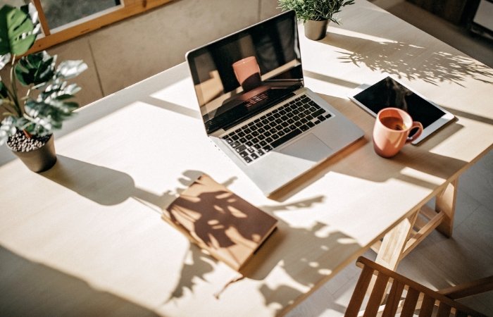 Light wooden table with an open laptop, a brown notebook, a steaming mug, and a tablet. Blog post featured image.