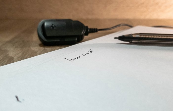 Page on a wooden desk with the word Interview written on it with a black pen and black microphone. Blog post featured image.