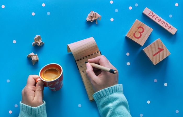 Person sitting and making a list while drinking espresso surrounded by scattered folded up pieces of paper.