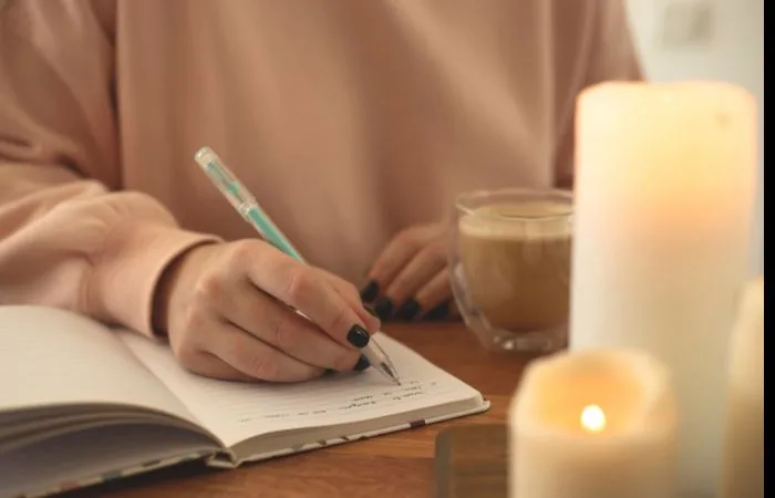 Women writing in a notebook with lit candles in the foreground.