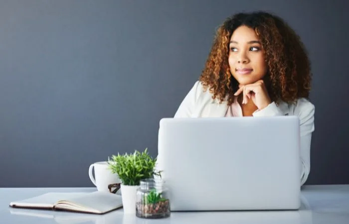 Girl sitting pensive by a laptop with grey background.